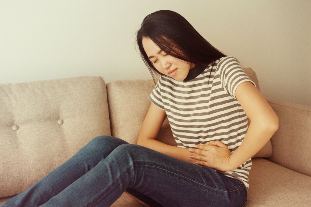 Young woman experiencing nausea, clutching her stomach, a symptom of chikungunya.