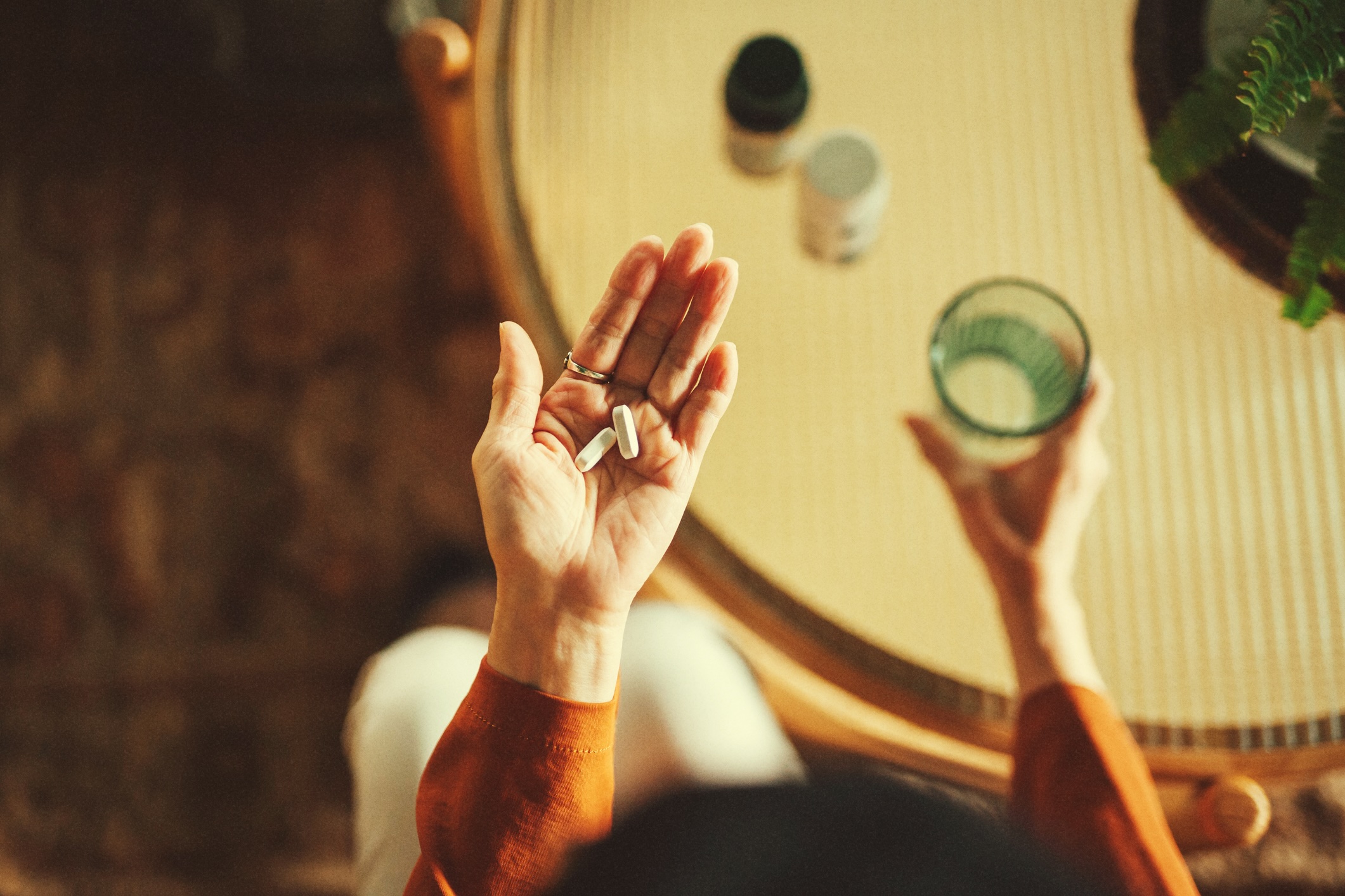 Person holding pills in one hand and glass of water in the other.