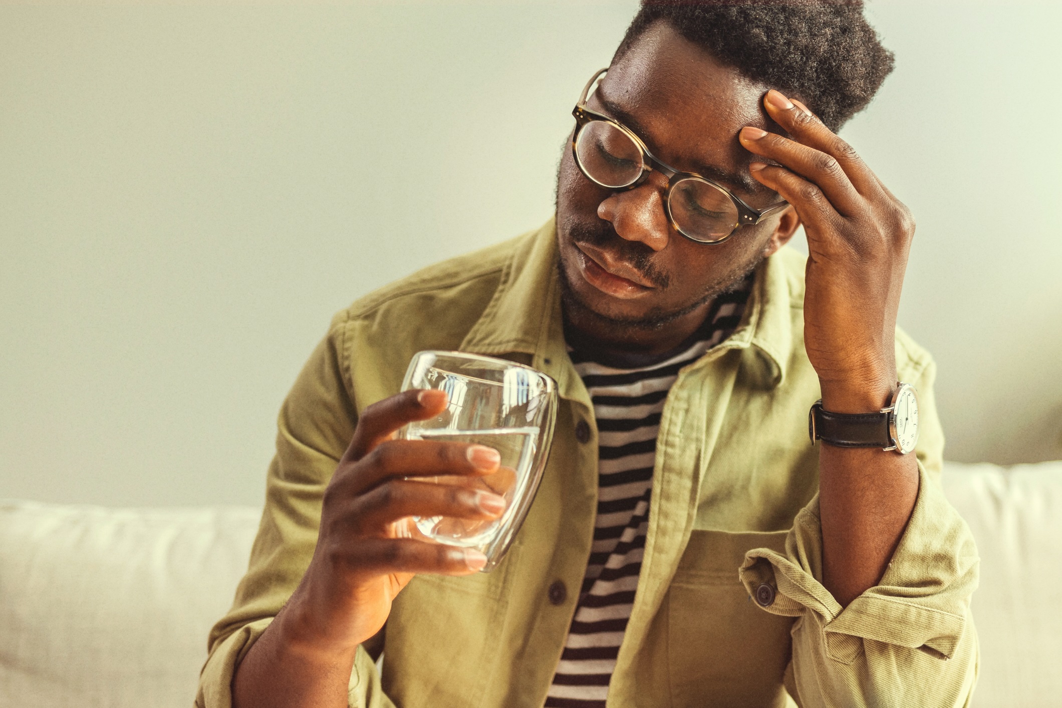 Person holding pills in one hand and glass of water in the other.
